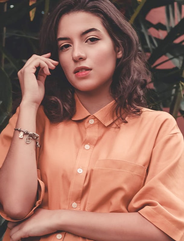 photo of a woman in an orange shirt with plants behind her