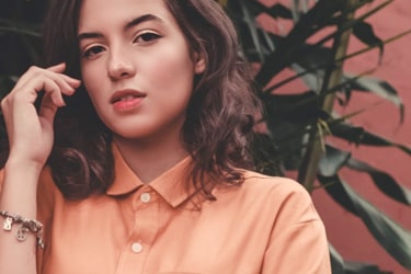 photo of a woman in an orange shirt with plants behind her